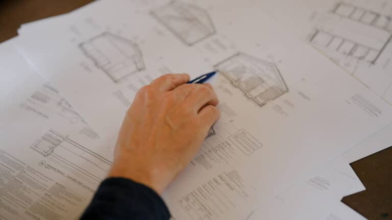 Mans hand holding pen over architectural drawings